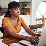 Young Woman Focused on Laptop and Paperwork at Home - GettyImages