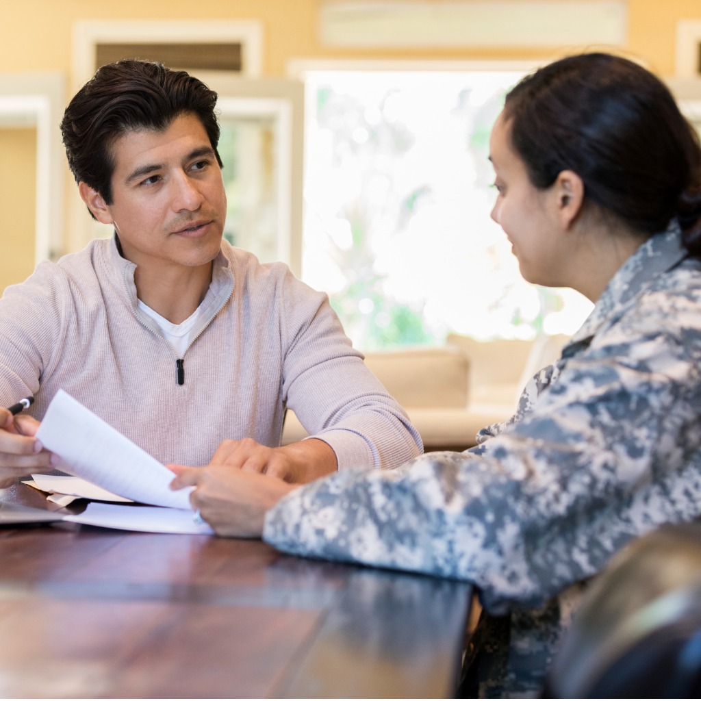 Woman in uniform sits at a table with a man as they look through papers